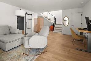 Ein modernes Wohnzimmer mit einer Couch, einem Schaukelstuhl, einem Schreibtisch mit Computer sowie einer Treppe und einer Tür.