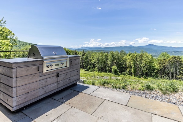 A wooden outdoor grill with a view of a forest and mountains.