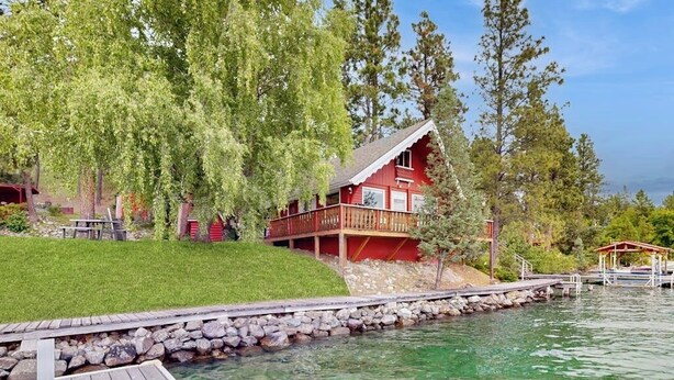 Un chalet au bord du lac, doté d’une terrasse en bois, d’un mur en pierre et d’une jetée qui s’avance dans l’eau.