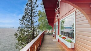 Une terrasse en bois avec une rambarde, une table et des chaises, d’où l’on peut admirer un plan d’eau et des arbres.