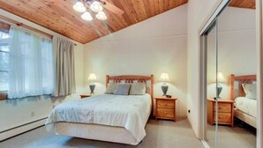 Una camera da letto con soffitto in legno, un letto con copripiumino bianco, due comodini con lampade e un'ampia finestra con tende.