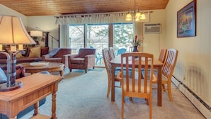 Un accogliente soggiorno con soffitto in legno, un tavolo da pranzo con sedie, un divano, una lampada e vista dalla finestra.