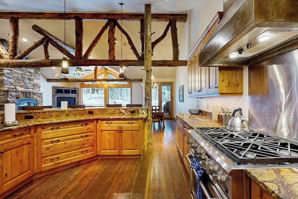 Une cuisine spacieuse avec des meubles en bois, un grand îlot central, une cuisinière à gaz et des poutres apparentes.