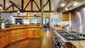 A spacious kitchen with wooden cabinets, a large island, a gas stove, and exposed wooden beams.