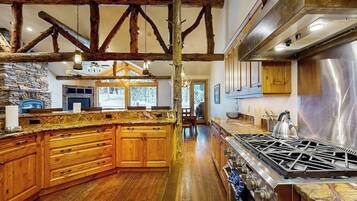 Une cuisine spacieuse avec des meubles en bois, un grand îlot central, une cuisinière à gaz et des poutres apparentes.