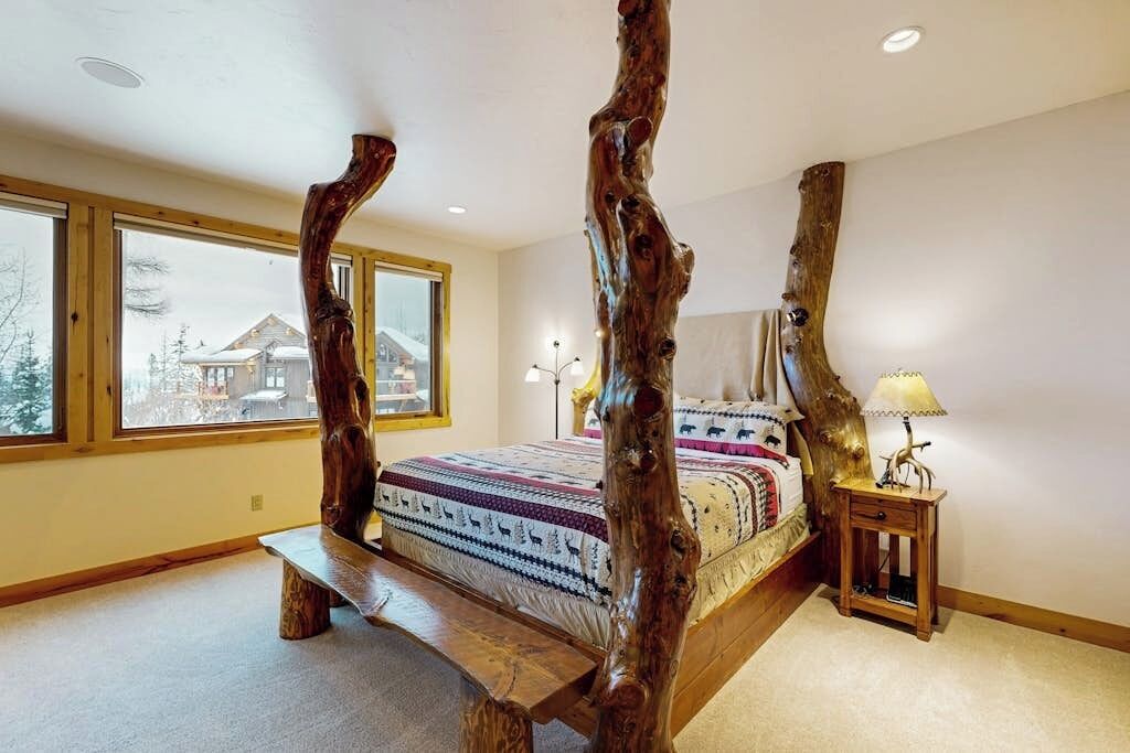 Une chambre à coucher avec un lit à baldaquin, de grandes fenêtres et une vue sur une maison à l’extérieur.