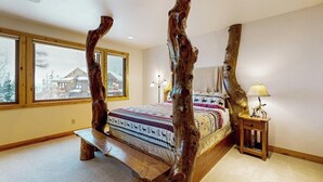A bedroom with a four-poster bed, large windows, and a view of a house outside.
