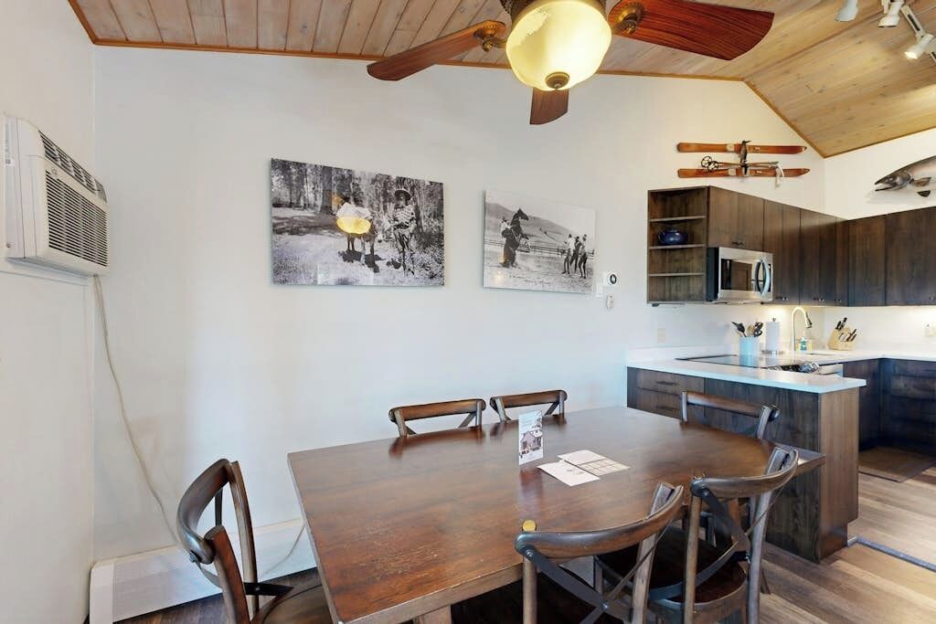 Un espace repas comprenant une table et des chaises en bois, un ventilateur de plafond et des œuvres d’art accrochées aux murs.