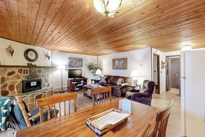 A cozy living room with a stone fireplace, wooden ceiling, and a dining area with a wooden table and chairs.