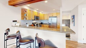 A modern kitchen with wooden cabinets, a stainless steel refrigerator, and a bar area with stools.