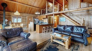 Un intérieur spacieux de chalet en bois, comprenant un coin repas, une cuisine et un salon avec des canapés en cuir.