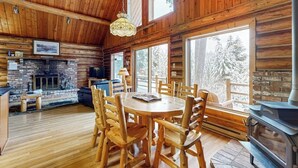 L’intérieur d’une cabane en rondins, avec une cheminée, une table à manger et de grandes fenêtres.