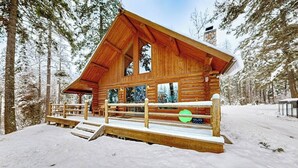 Une cabane en rondins avec une terrasse en bois, de grandes fenêtres et une cheminée en pierre.