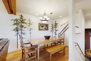 Ein Essbereich mit Holztisch, Stühlen, einer Bank, einer Chandelüstere und einer Treppe.