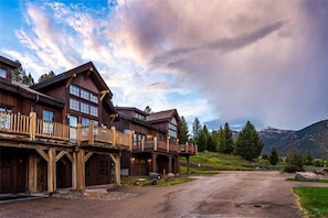 Ein großes Holzhaus mit mehreren Balkonen und einer Auffahrt mit Blick auf die Berge.