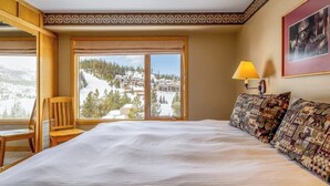 Quarto de hotel com uma cama grande, uma cadeira, uma janela com vista para uma paisagem nevada e um abajur.