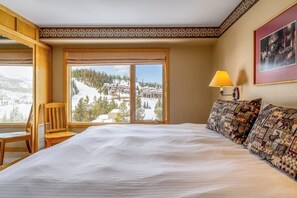 A hotel room with a large bed, a chair, a window with a view of a snowy landscape, and a lamp. - Mountain-view condo with heated hot tub, pool, sauna & easy access to slopes (Big Sky)