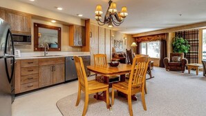 Uma cozinha com armários de madeira, uma mesa de jantar com cadeiras, um candelabro e uma janela grande com cortinas.