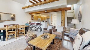 A spacious living area with a wooden dining table, leather sofas, and a kitchen in the background. - Slopeside townhome with ski-in/ski-out and private hot tub (Big Sky)