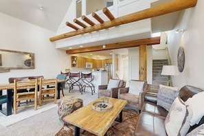 A spacious living area with a wooden dining table, leather sofas, and a kitchen in the background. - Slopeside townhome with ski-in/ski-out and private hot tub (Big Sky)