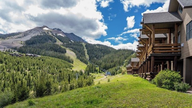 A mountain lodge with a ski lift, surrounded by forested hills and a clear sky. - Slopeside townhome with ski-in/ski-out and private hot tub (Big Sky)