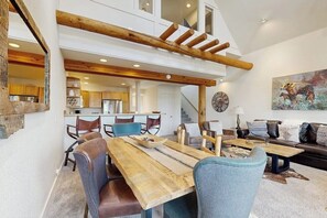 A dining area with a wooden table and chairs, a staircase, and a living room with a sofa and a painting. - Slopeside townhome with ski-in/ski-out and private hot tub (Big Sky)