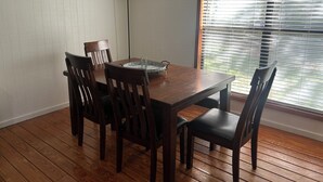 Een eetgedeelte met een houten tafel, vier stoelen, een vloerlamp en een raam met zonwering.