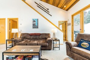 A cozy living room with a brown leather sofa, a coffee table with magazines, and a wooden ceiling. - Ski-in/ski-out townhome steps from Bear Back lift w/free WiFi & wood fireplace (Big Sky)