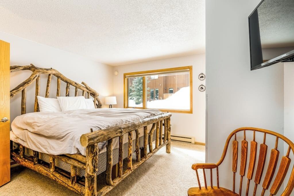 A bedroom with a rustic wooden bed, a window with a view of snow, and a television mounted on the wall.