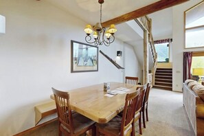 A dining area with a wooden table, chairs, a chandelier, a staircase, and a sofa. - Ski-in/ski-out mountaintop getaway with private hot tub - close to town (Whitefish)