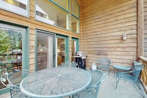 Portico esterno coperto con tavoli e sedie in metallo, un barbecue e vista sull'interno attraverso ampie finestre.