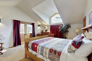 Una camera da letto con soffitto a falde, un letto con copripiumino decorato, una cassettiera, una scrivania, una ventola e una finestra con tende.
