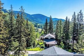 Ein Haus, umgeben von hohen Nadelbäumen, mit einer Bergkette im Hintergrund.
