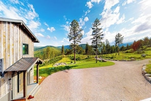 A wooden cabin with a gravel driveway and a view of a forested landscape. - Gorgeous lake-view cabin with game room & fireplaces - near Blacktail Mountain (Lakeside)