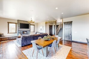 Un amplio espacio de estar con una mesa de comedor de madera, asientos cómodos, un televisor grande y una escalera que sube a otro nivel.
