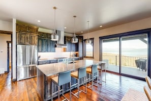 Una cocina moderna con una isla central, taburetes de bar, electrodomésticos de acero inoxidable y vistas a un balcón.
