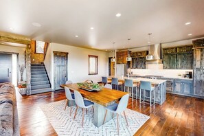 Una cocina amplia con una isla central, iluminación colgante moderna y una escalera rústica.