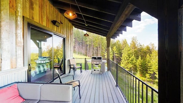 Eine Holzterrasse mit Grill, Sitzgelegenheiten und Blick auf Bäume.