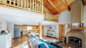 A spacious living area with a high ceiling, a fireplace, a dining area, and a kitchen. - Secluded lodge w/ spacious deck, wood-burning stove, full kitchen, & free WiFi (Whitefish)