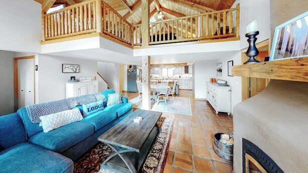 A spacious living area with a high ceiling, a blue sofa, a wooden dining table, and a kitchen in the background. - Secluded lodge w/ spacious deck, wood-burning stove, full kitchen, & free WiFi (Whitefish)