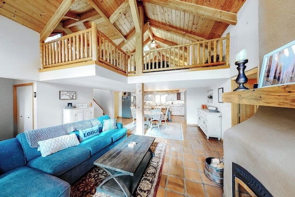 Ein geräumiger Wohnbereich mit hoher Decke, einem blauen Sofa, einem Holzesstisch und einer Küche im Hintergrund.