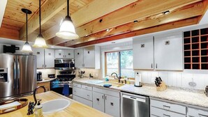 A modern kitchen with stainless steel appliances, wooden ceiling beams, and a large island with a sink. - Secluded lodge w/ spacious deck, wood-burning stove, full kitchen, & free WiFi (Whitefish)