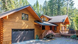A log cabin with a garage, a covered porch, and a staircase leading to a deck. - Secluded lodge w/ spacious deck, wood-burning stove, full kitchen, & free WiFi (Whitefish)
