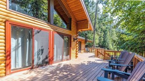 A log cabin with a deck, outdoor seating, and a forest backdrop. - Secluded lodge w/ spacious deck, wood-burning stove, full kitchen, & free WiFi (Whitefish)
