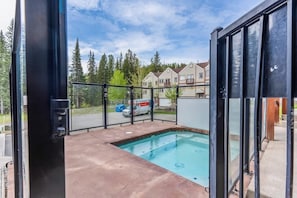Ein Poolbereich mit Glasveranda, einer Betonplattform und Blick auf Häuser und Bäume im Hintergrund.