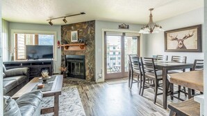 Una sala de estar con chimenea, televisor, comedor con sillas y un ventanal grande.