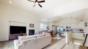 A modern living room with a sofa, TV, fireplace, and a kitchen area with cabinets and a dining table. - Charming home with mountain view, fireplace, balcony, & washer/dryer (Belgrade)