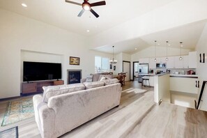 A modern living room with a sofa, TV, fireplace, and a kitchen area with cabinets and a dining table. - Charming home with mountain view, fireplace, balcony, & washer/dryer (Belgrade)