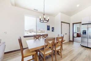 A dining area with a table and chairs, a chandelier, a refrigerator, and a view through a window. - Charming home with mountain view, fireplace, balcony, & washer/dryer (Belgrade)