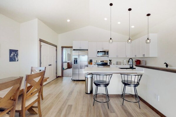 A modern kitchen with white cabinets, stainless steel appliances, and a central island with bar stools. - Charming home with mountain view, fireplace, balcony, & washer/dryer (Belgrade)